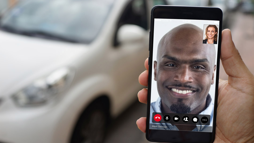 man holding a phone doing video conferencing with a car background
