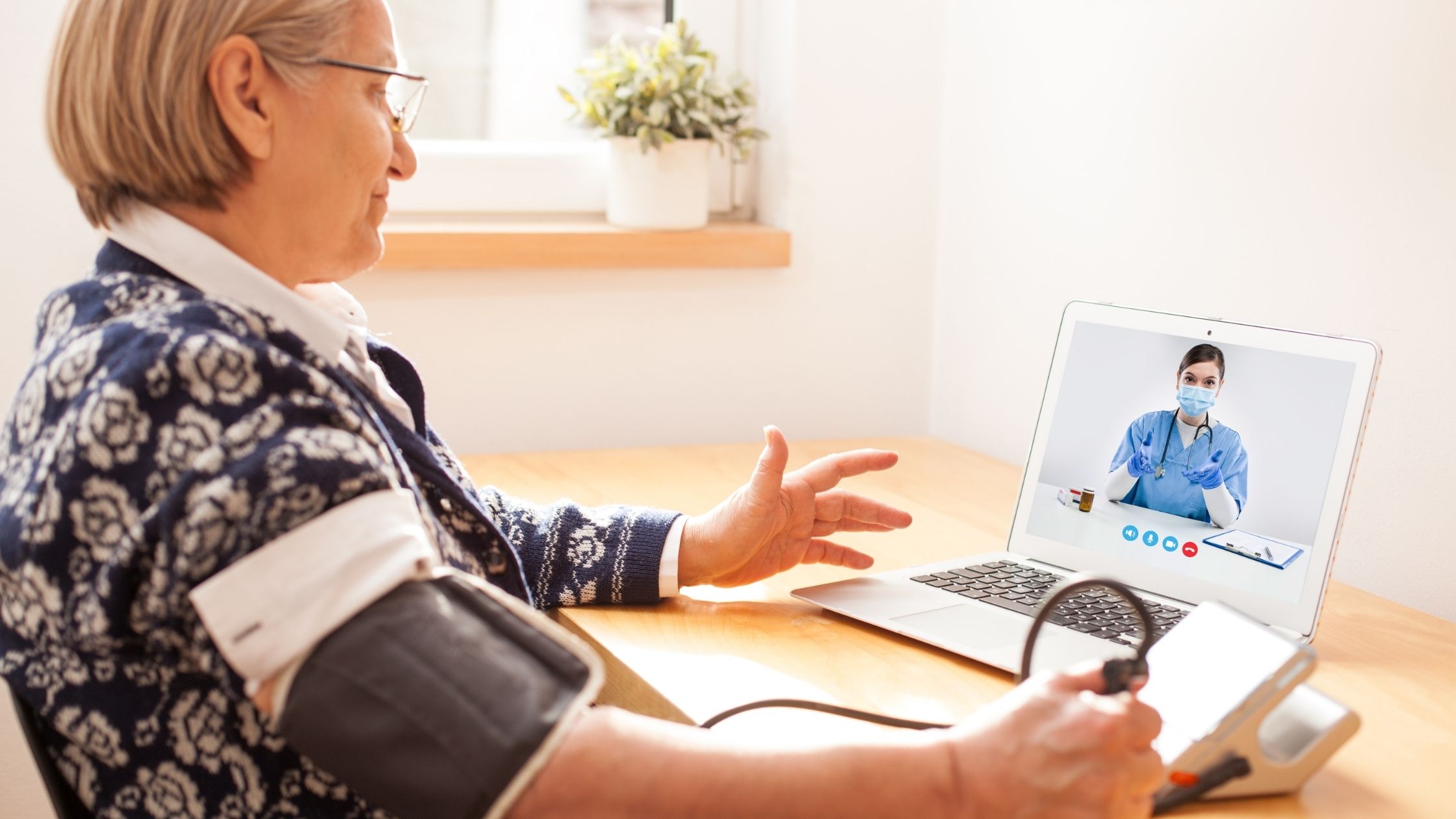 Oudere gepensioneerde vrouw die de bloeddrukmonitor van de sfygmomanometer gebruikt om hartslagpules te meten, sprekend aan vrouwelijke e-arts via online de hulplijn van de videogespreksoproep, zelf-controlerende verre telegeneeskunde