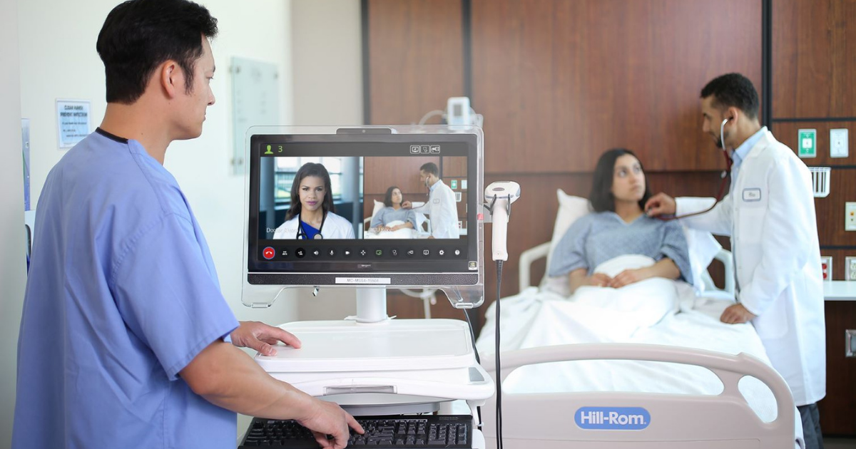 Medical staff treating patient laying in bed, while video calling a doctor. They are delivering patient care with medical carts.