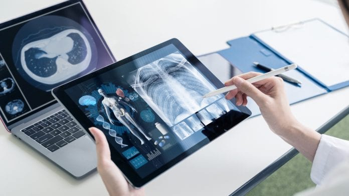 A doctor using tablet and laptop to access patient information