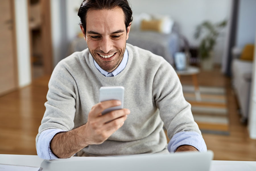 joven-empresario-feliz-trabajando-en-casa-mensaje-de-texto-teléfono-móvil