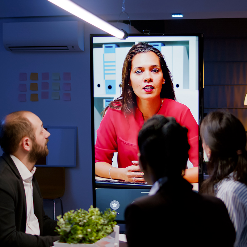 Office meeting with woman on monitor via video conference