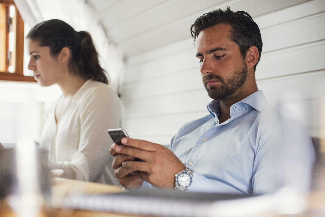 Midden volwassen zakenman die mobiele telefoon gebruikt door vrouwelijke collega op kantoor
